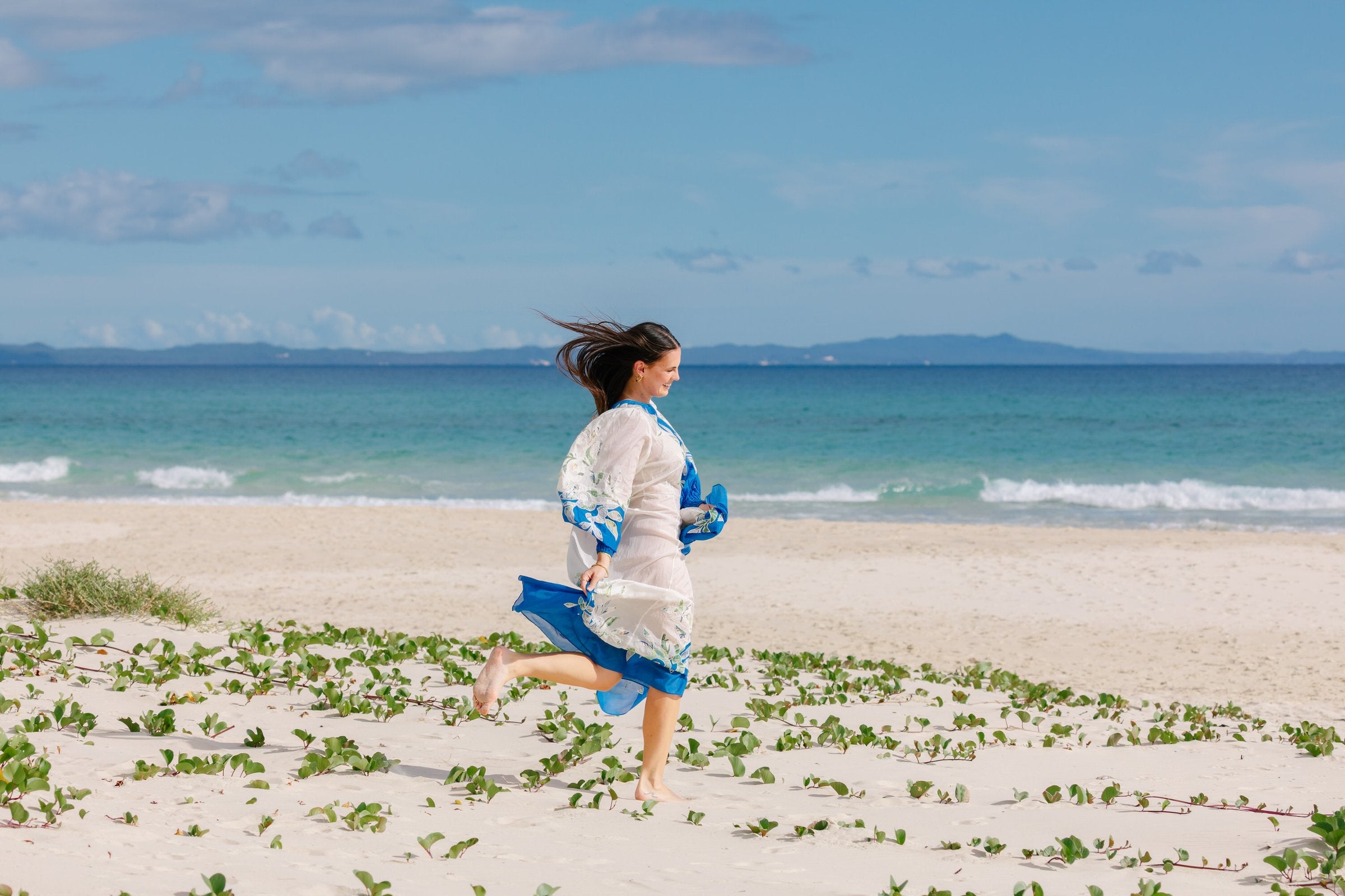 Woman running along the beach at North Stradbroke Island in a white and blue dress