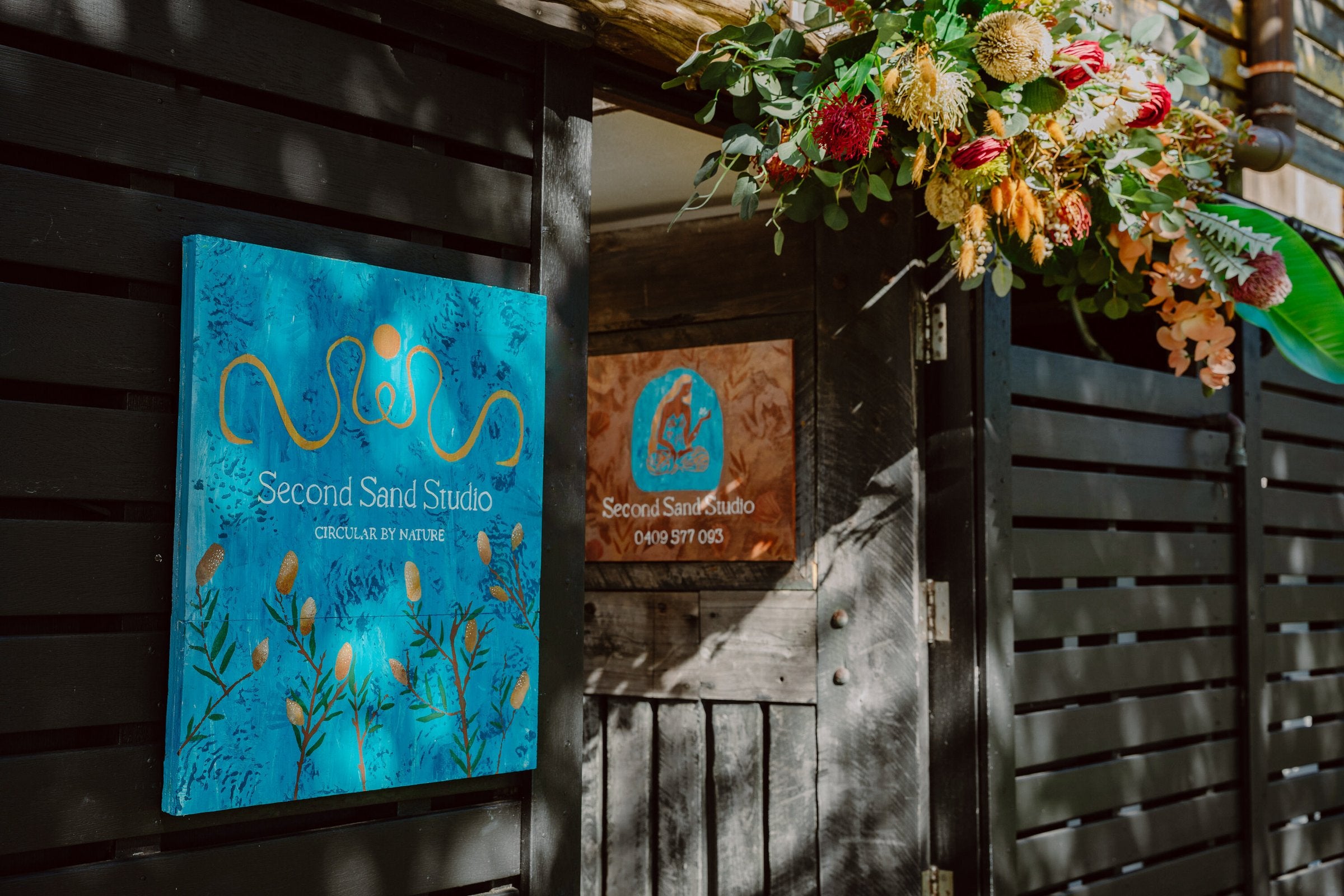 Second Sand Studio entrance with hand-painted sign and native flower arrangement, North Stradbroke Island